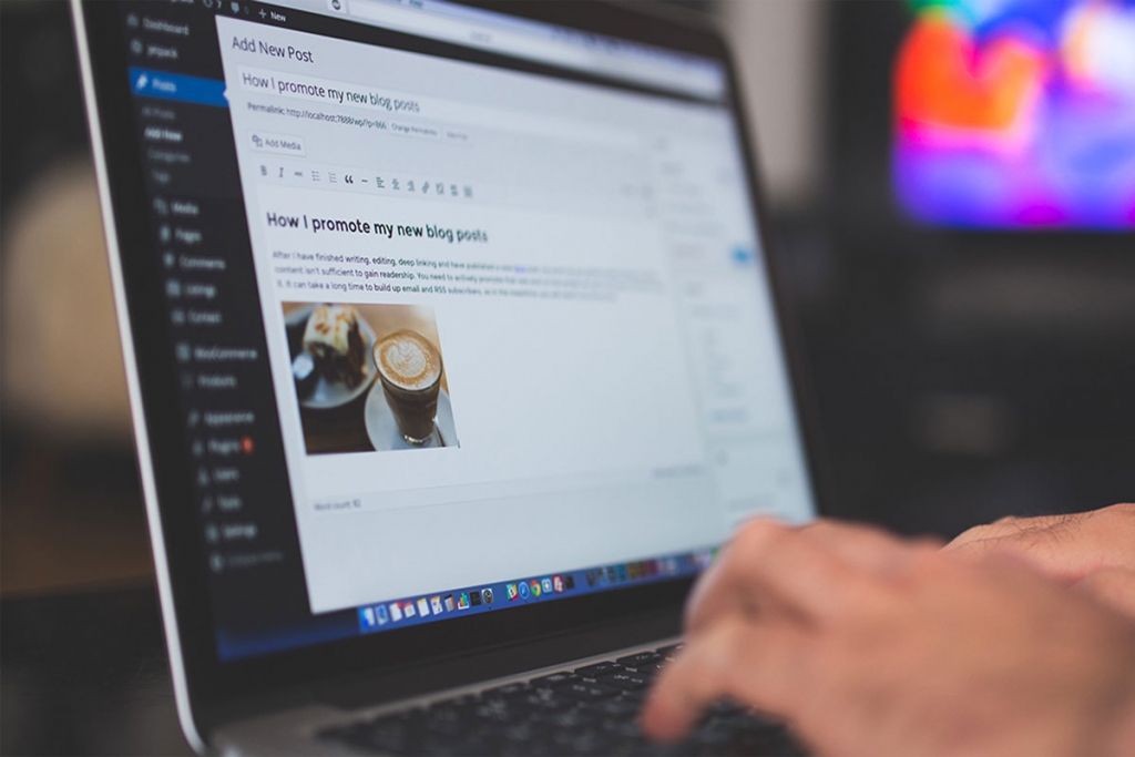 Roka na tipkovnici prenosnika z odprtim urejevalnikom objav v WordPressu